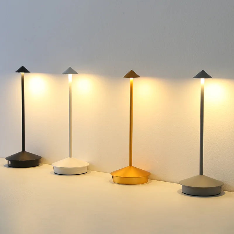 Vier schmale LED-Tischlampen in Schwarz, Gold und Grau leuchten nebeneinander

