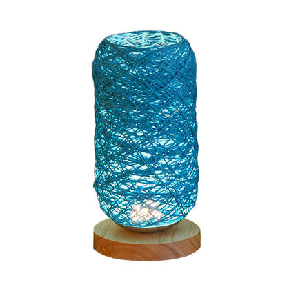 Geflochtene Tischlampe in Blau mit zylindrischer Form und Holzsockel vor hellem Hintergrund