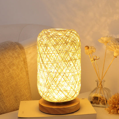 Gelbe Tischlampe mit geflochtenem Schirm auf Nachttisch neben Trockenblumen